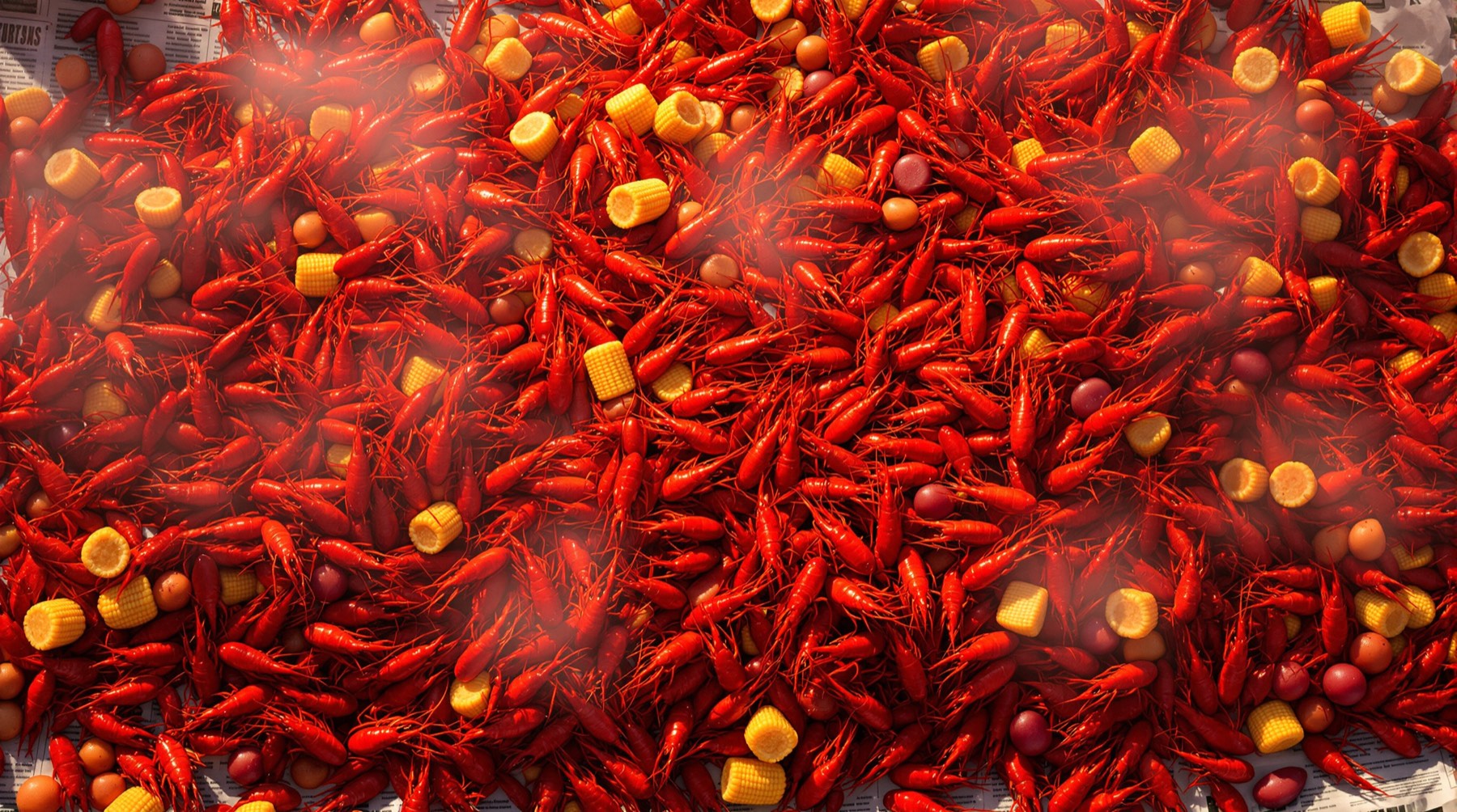 A crawfish boil dumped across a newspaper covered table with corn, potatoes and sausage, still steaming.
